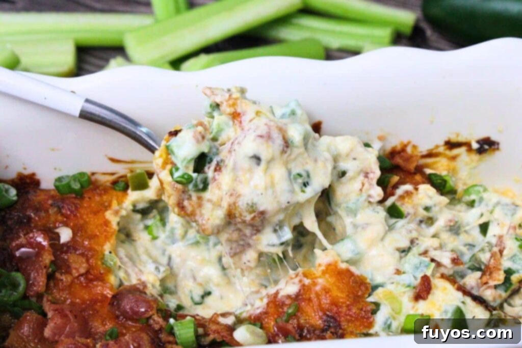 A spoonful of hot, gooey cheesy jalapeno popper dip being pulled from a baking dish.
