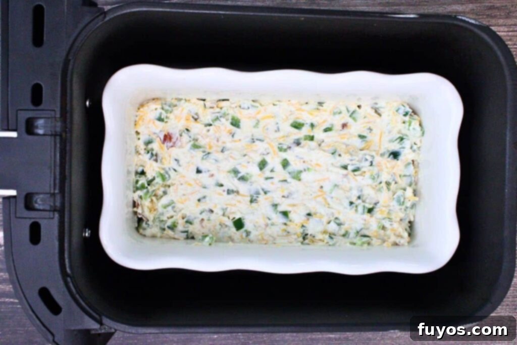Casserole dish with the jalapeno popper dip placed inside an air fryer basket, mid-cooking process.