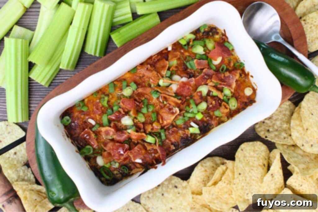 Overhead shot of the finished air fryer jalapeno dip, garnished with green onions and surrounded by celery sticks, tortilla chips, and a fresh jalapeno for serving.