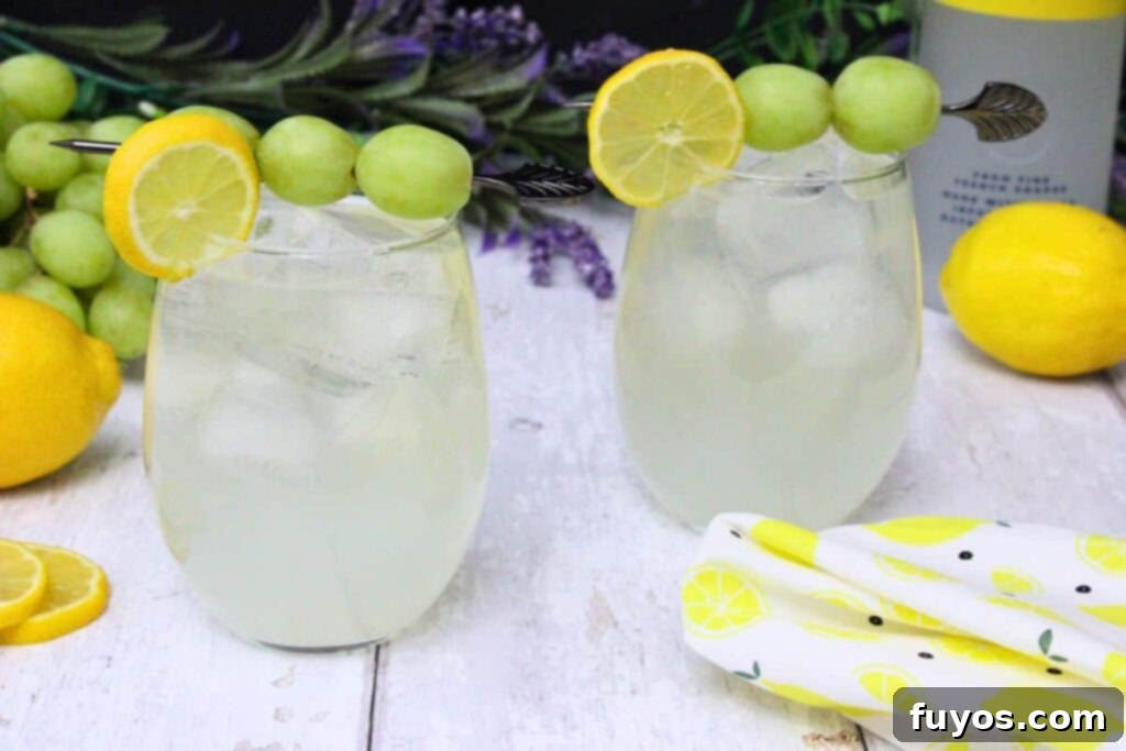 Zesty Sparkling Vodka Lemonade 8 Two vibrant vodka lemonade spritzers, garnished with lemon and grape skewers, on a white wooden table.