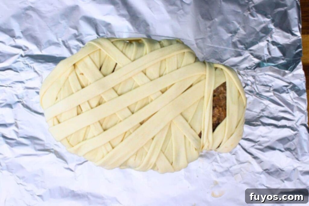 Spooky Halloween Air Fryer Mummy Meatloaf 10 transfer partially cooked meatloaf on top of crescent dough and wrap strips as bandages around the mummy