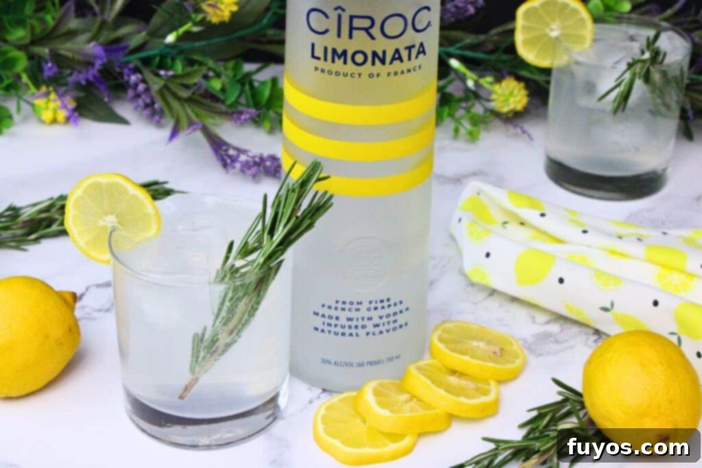 sparkling lemonade cocktail with a sprig of rosemary and fresh lemons next to a tall vodka bottle