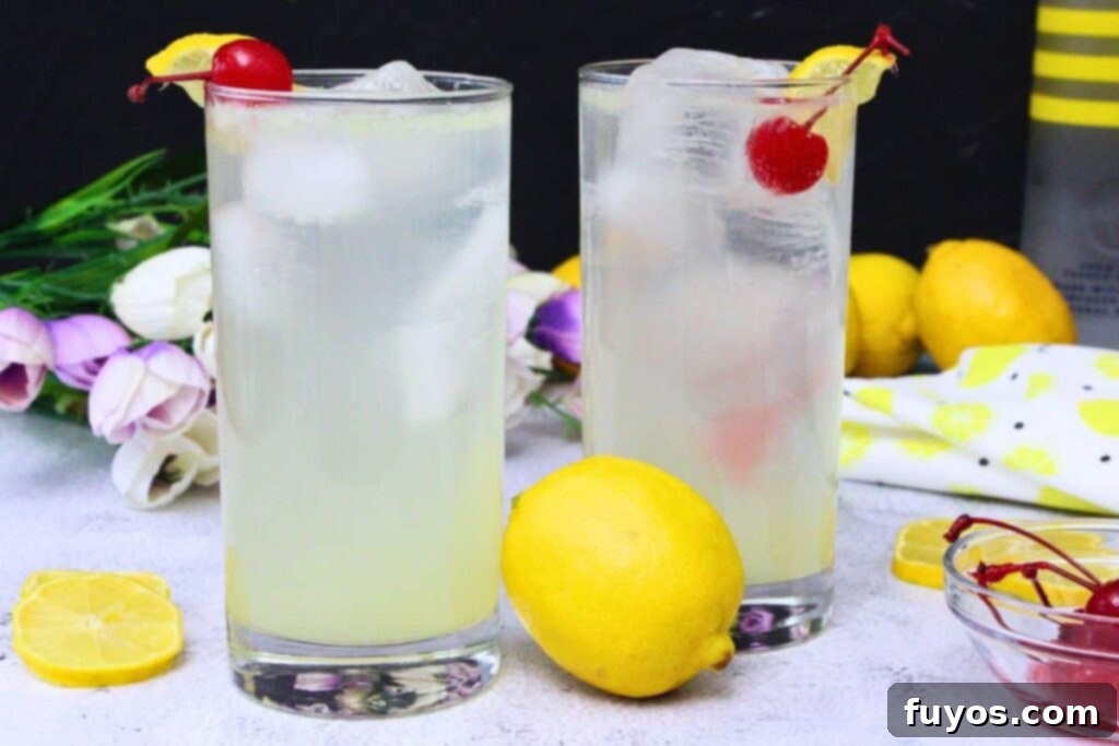 Lemon Vodka Collins: Summer's Zesty Escape 3 Two tall Lemon Vodka Collins drinks garnished with lemon slices and maraschino cherries on a table with fresh lemons