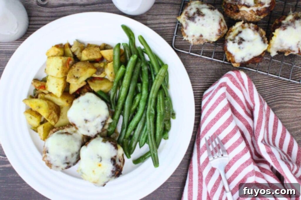 overhead view of cheesy meatloaf muffins on a plate with potatoes and green beans next to a napkin and fork