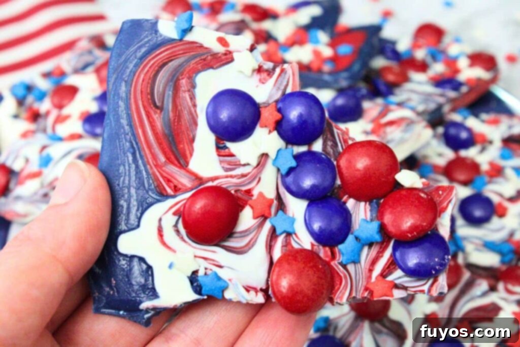 Red, White, and Blue Bark: Your Festive Fourth of July Dessert 3 holding up a piece of fourth of july bark with red and blue chocolate candy