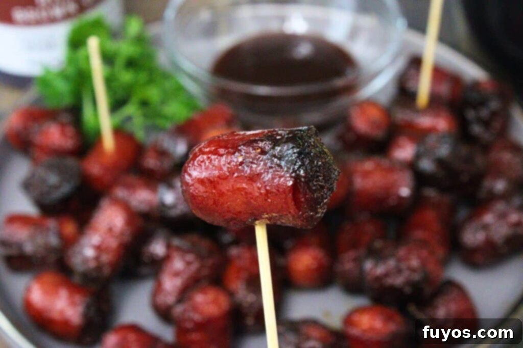Air Fryer Hot Dog Burnt Ends A Speedy BBQ Spin 3 holding up a hot dog burnt end on a toothpick in front of more burnt ends and bbq sauce