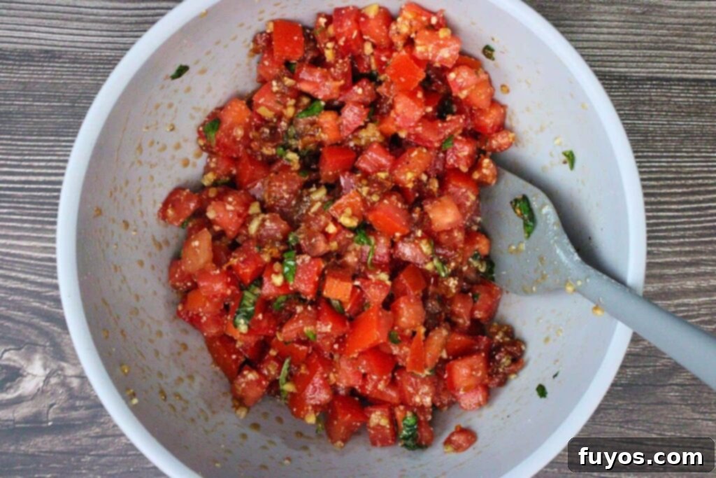Combining fresh diced tomatoes, garlic, sun-dried tomatoes, olive oil, basil, balsamic, and Parmesan in a bowl