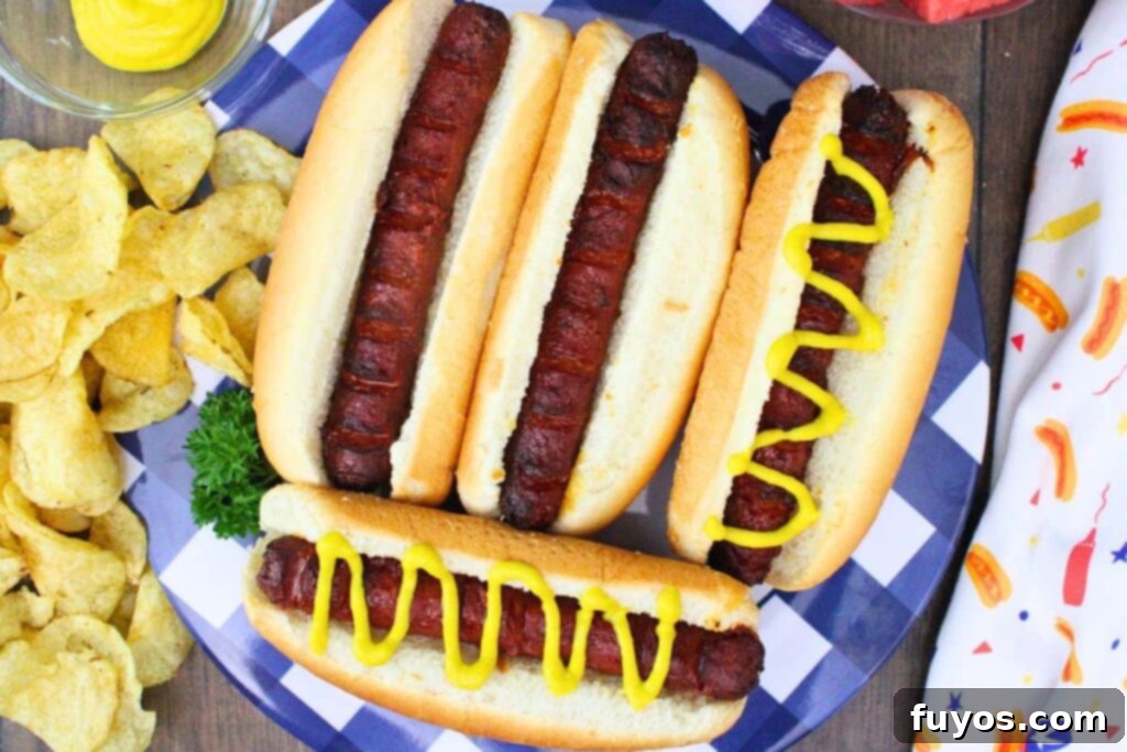 Flavor-Packed Air Fryer Franks 8 overhead view of four marinated hot dogs on a plate with two topped with mustard and chips on the side