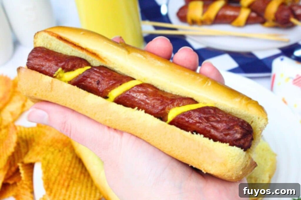 Air Fryer Crispy Spiral Hot Dogs 3 holding a spiral hot dog made in the air fryer with mustard laying in the spiral grooves
