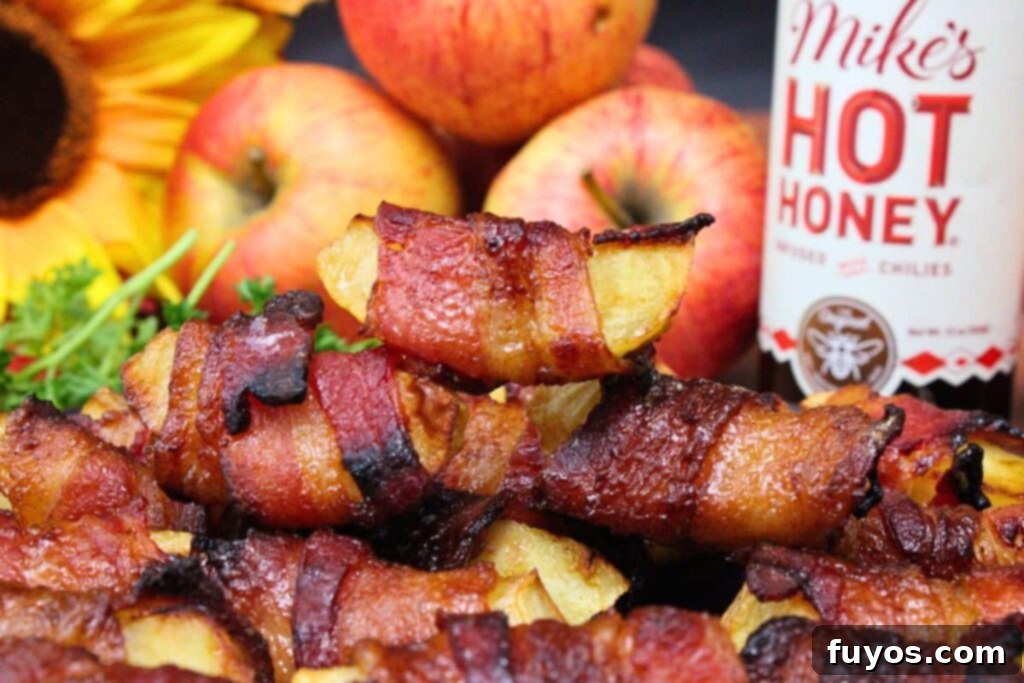 Sweet and Savory Air Fryer Bacon Apple Bites 3 closeup view of air fryer bacon wrapped apples stacked up with a bottle of hot honey in the background