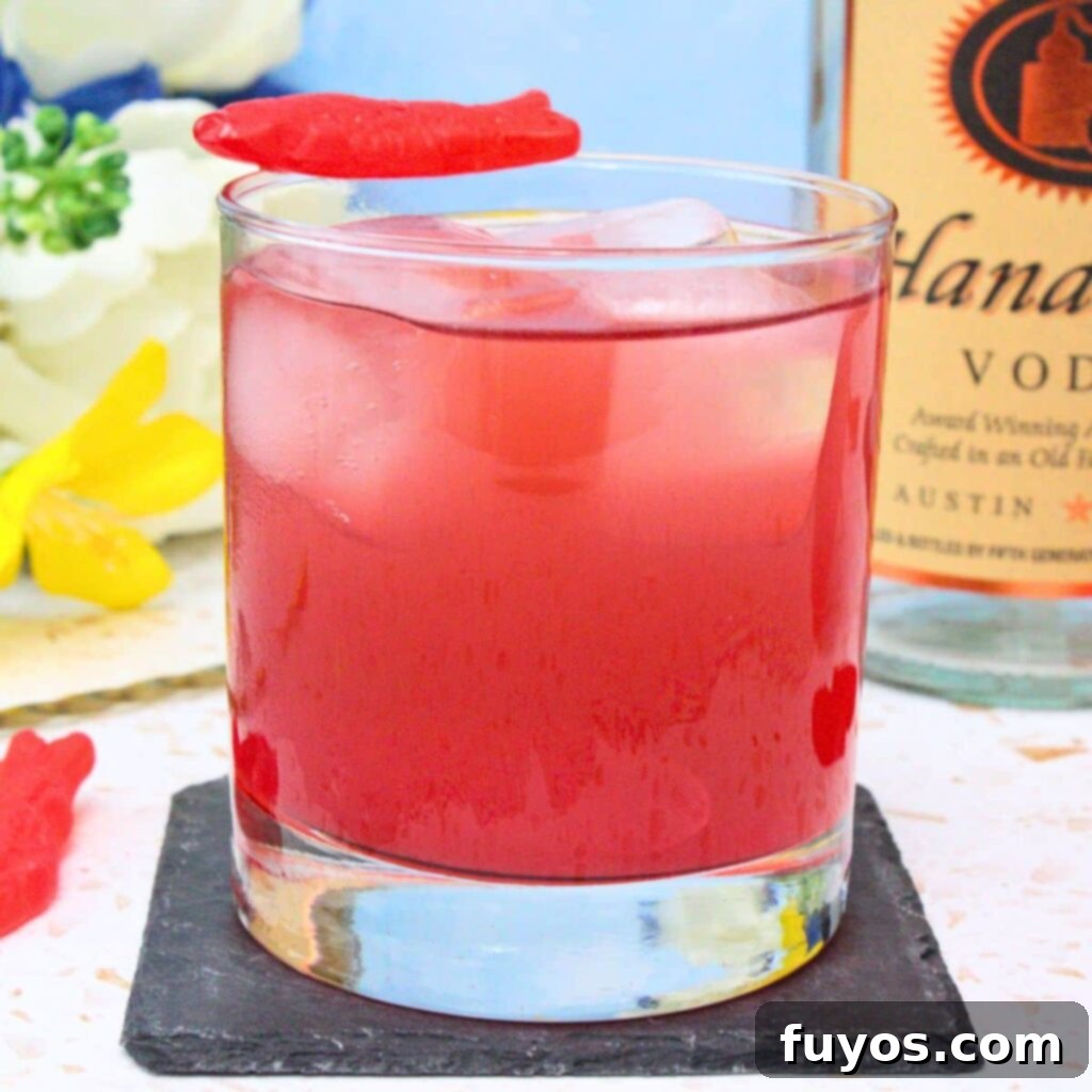 Vibrant red Swedish Fish cocktail with gummy candies and a clear vodka bottle on a light, summery background.
