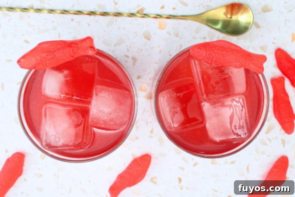An inviting overhead view of two perfectly garnished Swedish Fish cocktails, surrounded by gummy candies and a cocktail stirrer.
