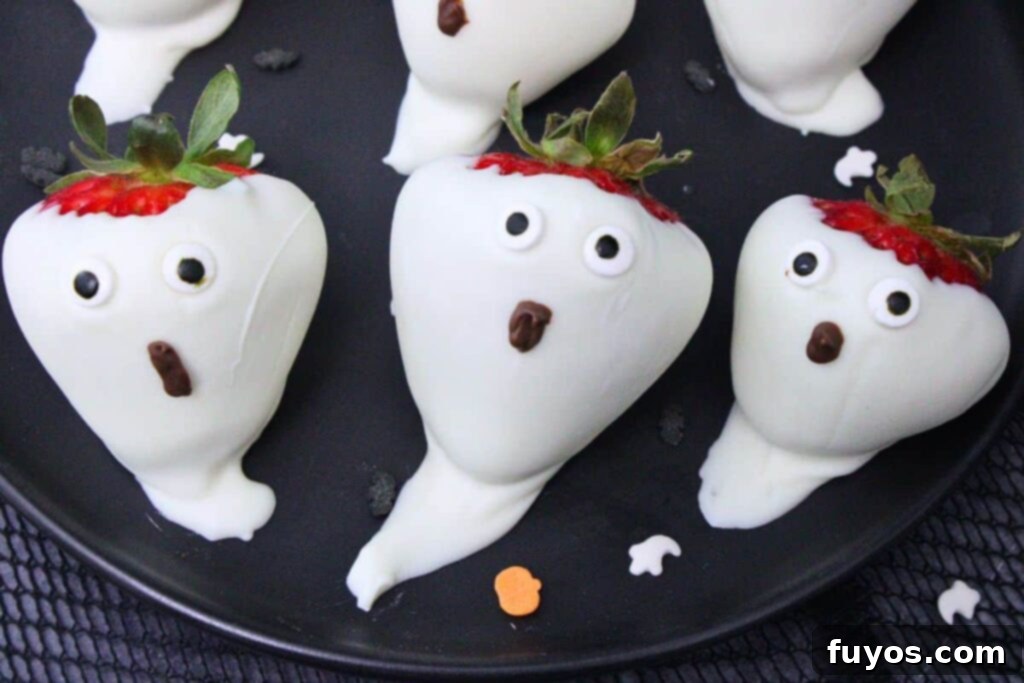 three strawberry ghosts with candy eyes and chocolate mouths on a black plate
