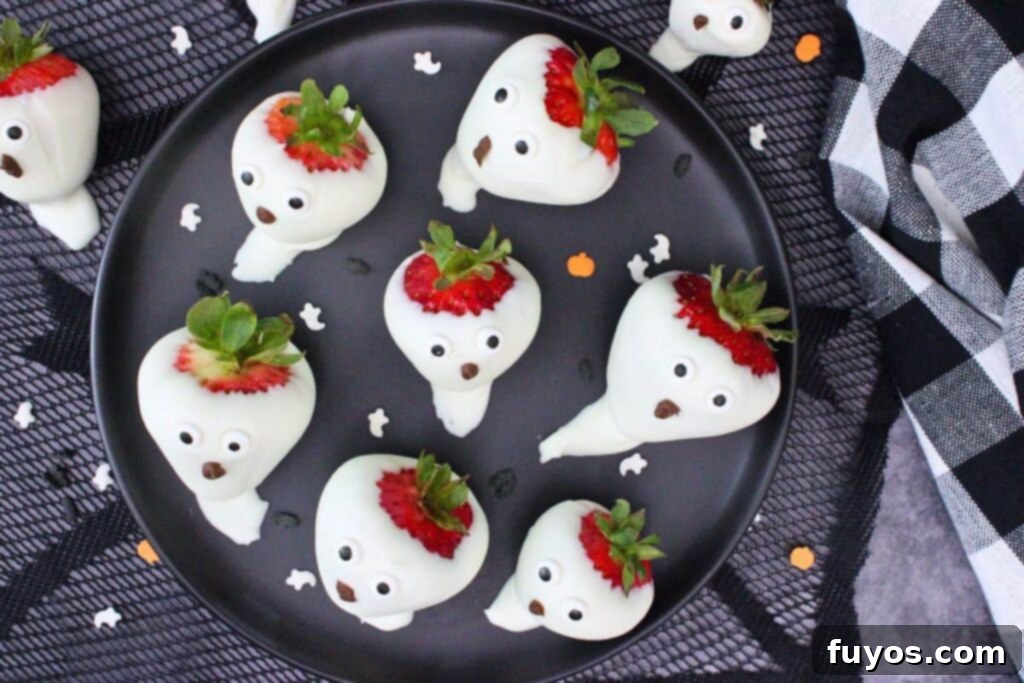 overhead view of several chocolate strawberry ghosts on a black plate on a spiderweb mat