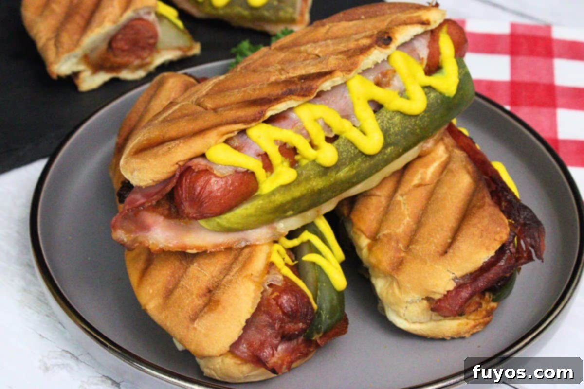 27 Irresistible Air Fryer Hot Dog Creations 12 three cuban hot dogs on a plate showing off pickle spear, mustard swirl, and panini grill marks