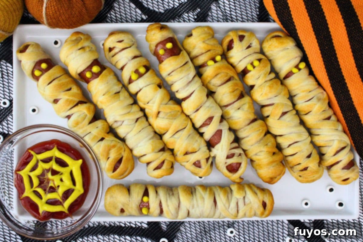 27 Irresistible Air Fryer Hot Dog Creations 14 overhead view of air fryer mummy hot dogs laid across a platter with a spiderweb mix of ketchup and mustard