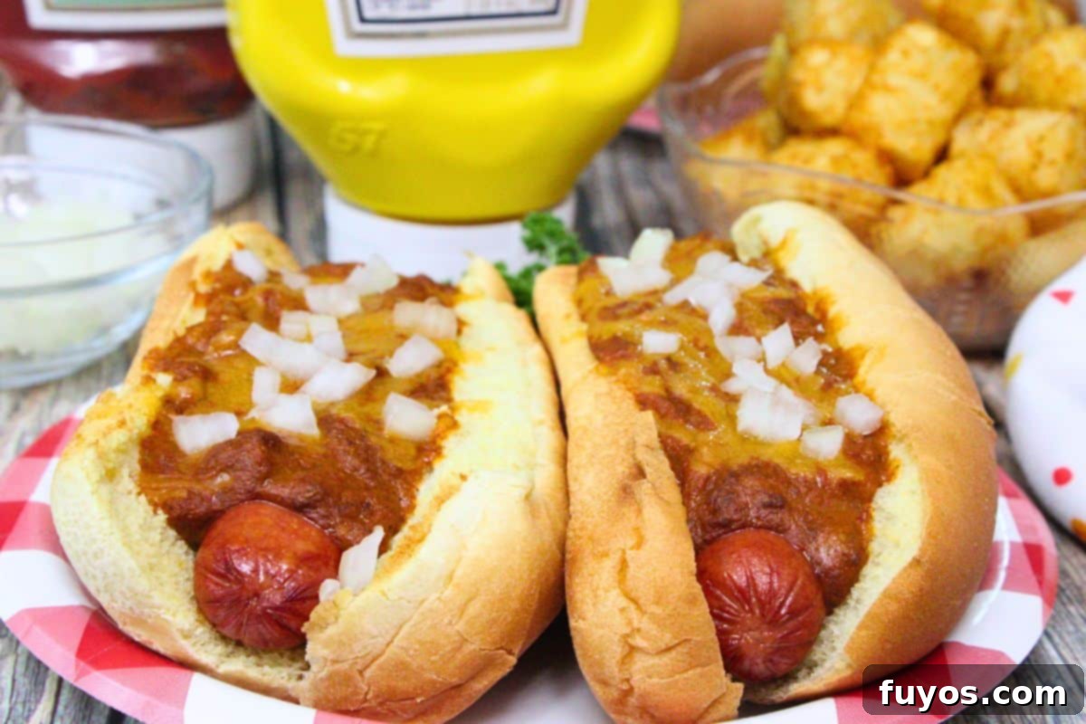27 Irresistible Air Fryer Hot Dog Creations 4 two sonic chili cheese dogs topped with onions side by side in front of ketchup, mustard, and tater tots