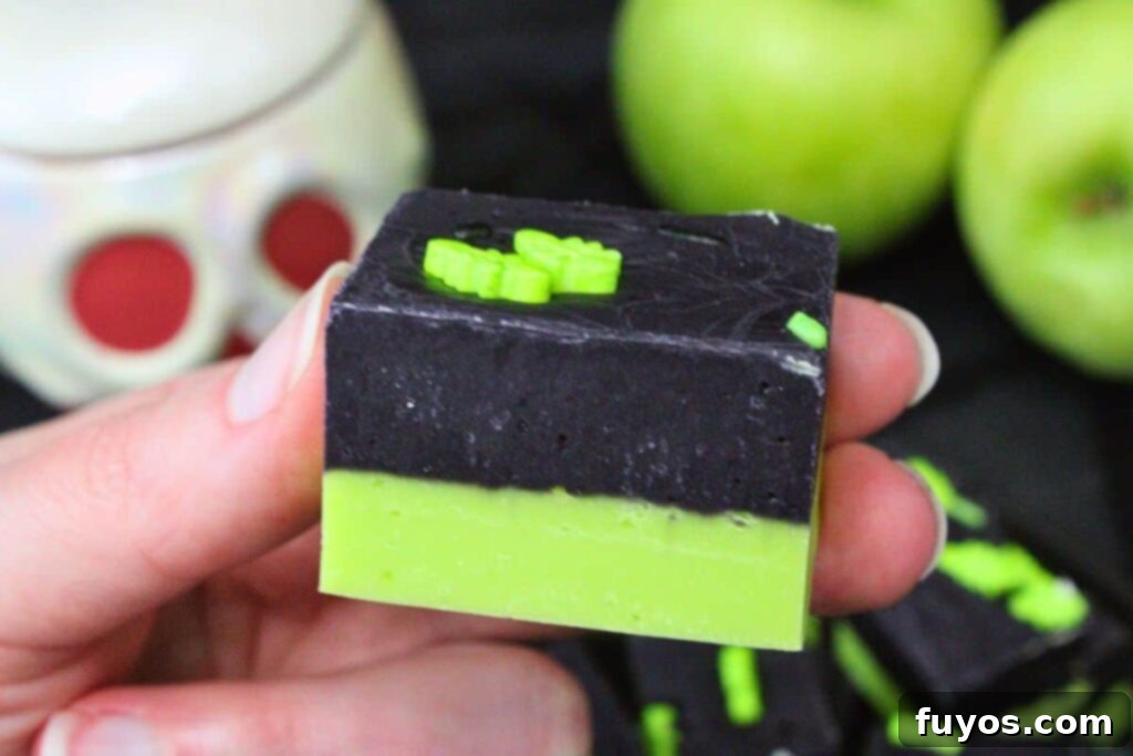 Poison Apple Fudge: A Hauntingly Easy No-Bake Treat 3 holding up a square of poison apple fudge showing the green and black layers