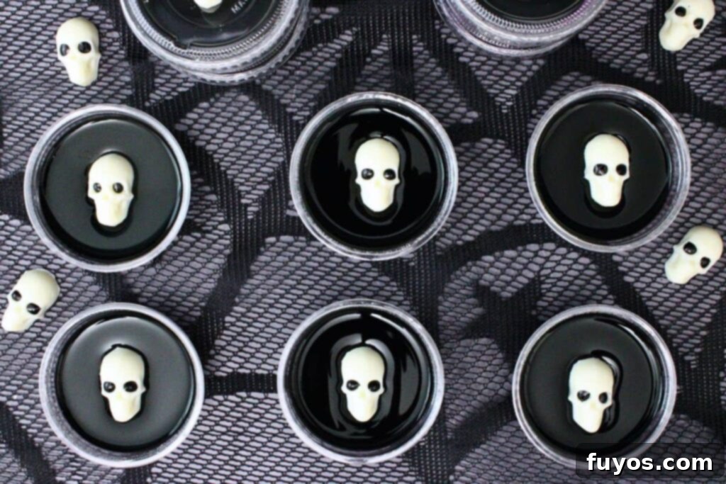 overhead view of several black jello shots topped with a white chocolate skull on a lace black web cloth