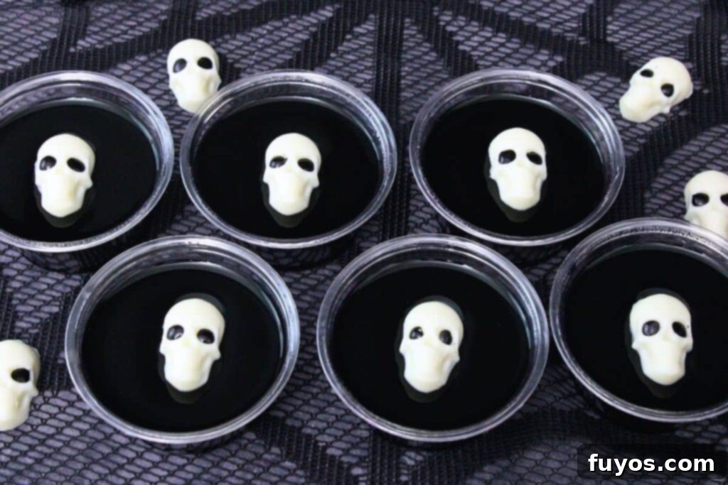 six black jello shots in two rows with a white chocolate skull on top of each