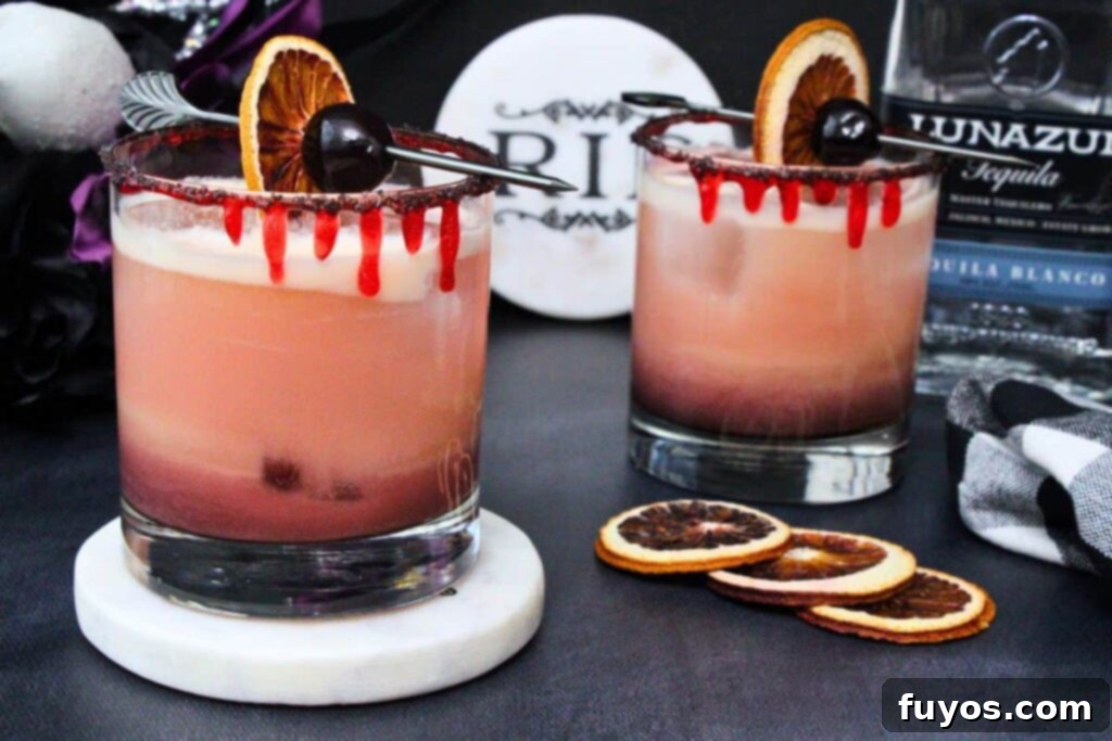 two bloody tequila sunset cocktails with one on a coaster and both garnished with blood orange and cherry amidst dark halloween scene