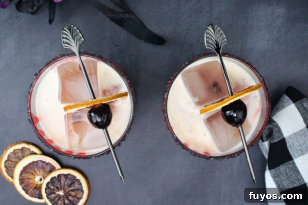 overhead view of two bloody tequila sunset drinks garnished with dried blood orange slice and cocktail cherry on a dark counter