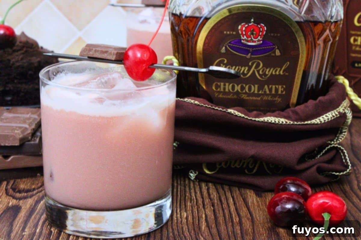 black forest cake cocktail with maraschino cherry next to chocolate crown royal bottle on a wooden table
