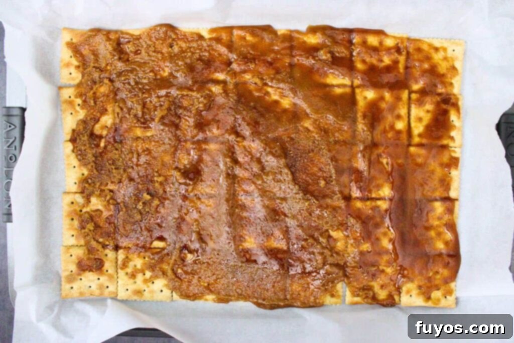 No Bake Halloween Saltine Crack Toffee 7 Pouring hot, molten sugar mixture over a base of saltine crackers on a baking sheet to create the toffee layer.