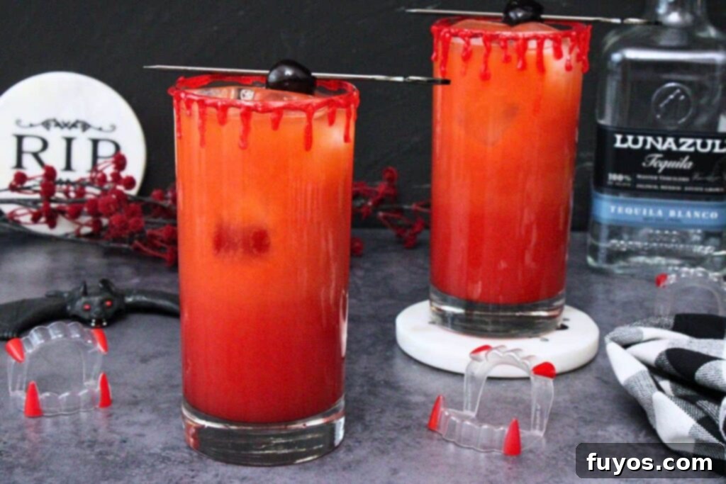 two vampire tequila sunrise cocktails with blood drip rim on a dark background with vampire teeth and bat decorations