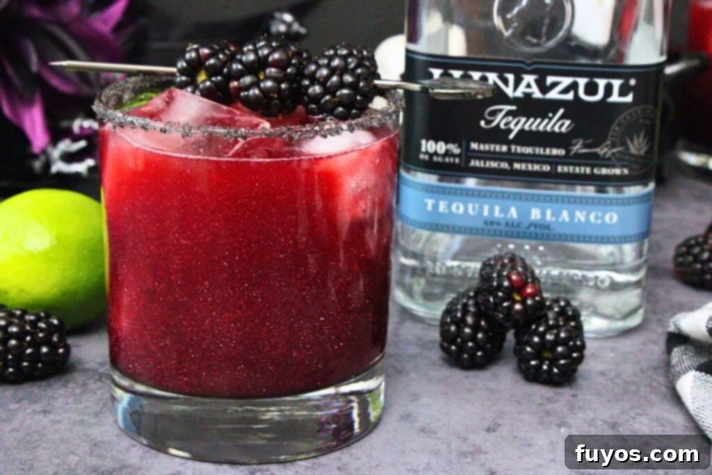 Disney's Spooky Black Magic Margarita 3 black magic margarita with blackberry skewer next to tequila bottle