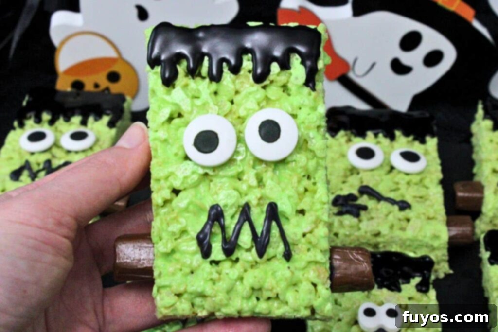 Conjure Up Frankenstein Krispie Monsters: No-Bake Halloween Magic 3 holding up a frankenstein rice krispie treat with big candy eyes, icing hair, and tootsie roll bolts