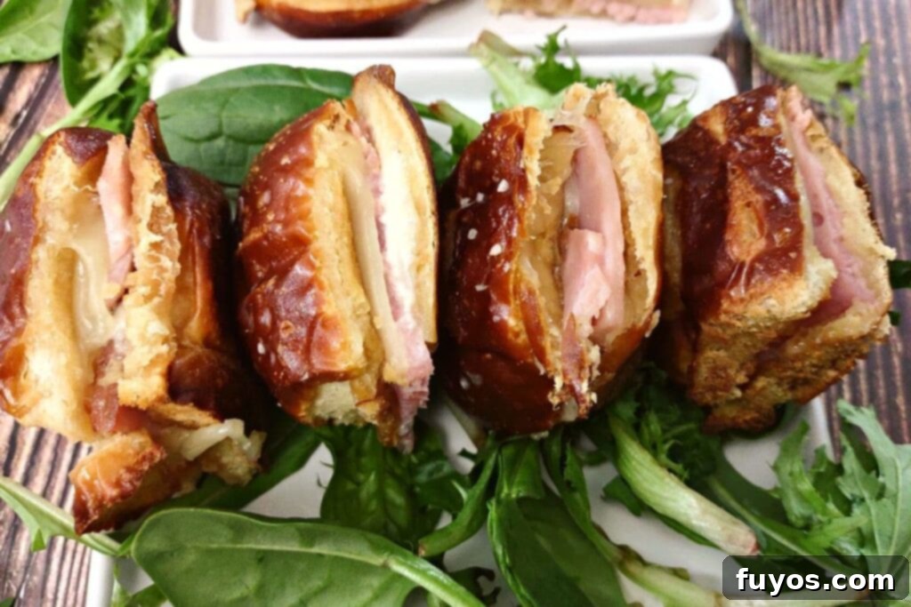 four ham and cheese sliders on their side sitting horizontal on a plate with greens
