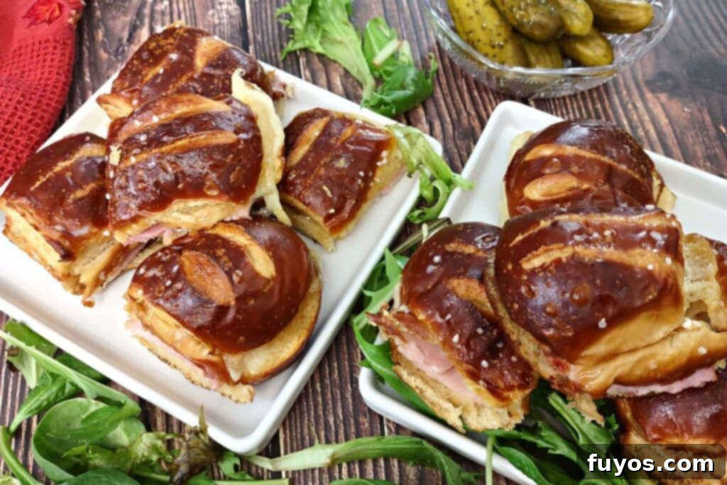 two plates of ham and cheese sliders on hawaiian pretzel rolls with pickles and greens