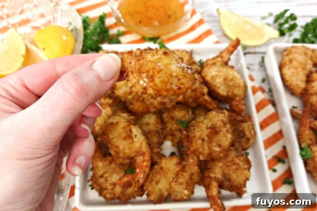 holding an air fried coconut shrimp dipped in duck sauce