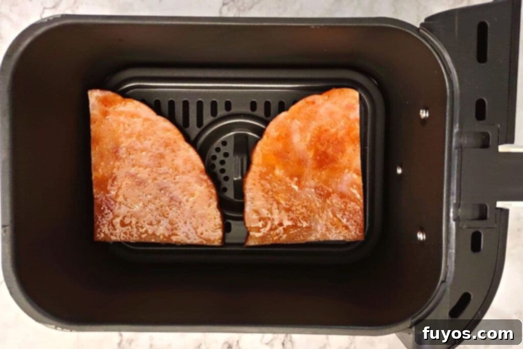 Ham steak in air fryer basket cooking