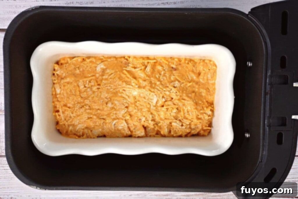 Ultimate Air Fryer Buffalo Chicken Dip 7 Dish with buffalo chicken dip placed inside the air fryer basket, ready to cook.
