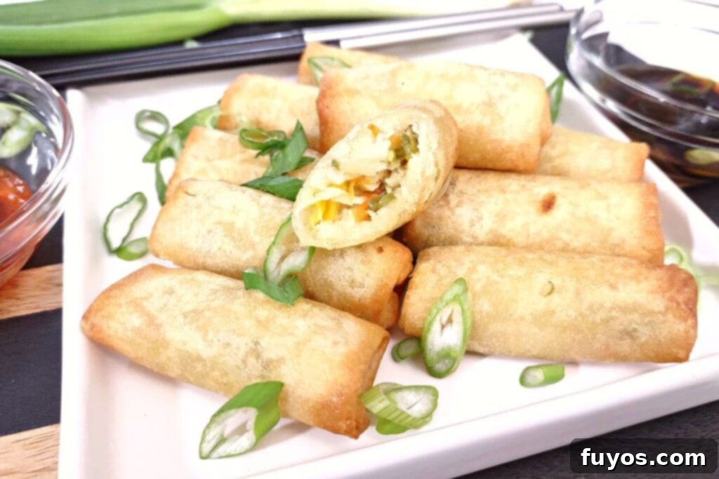 Crispy Air Fryer Spring Rolls in 5 Minutes 3 reheated air fryer spring rolls stacked on a plate with one cut in half