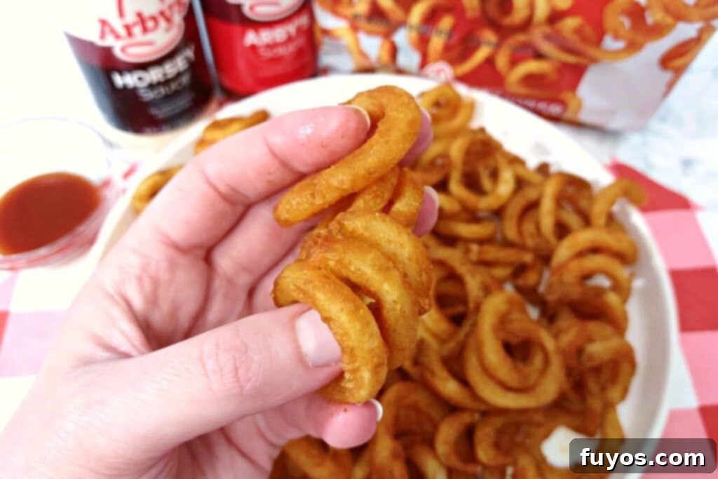 A hand holding a perfectly air fried Arby's curly fry, showcasing its golden-brown texture and appealing spiral shape.