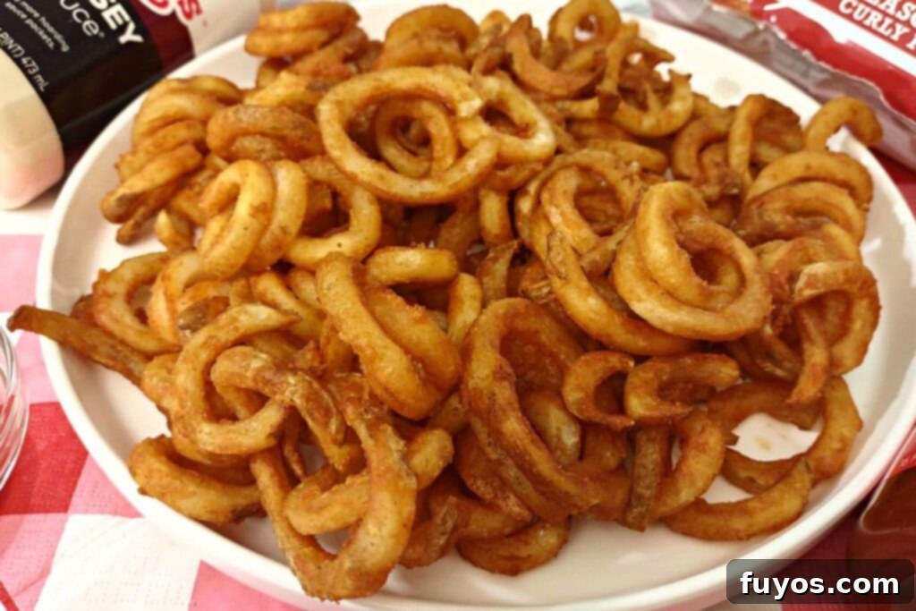 A close-up of quick frozen air fryer Arby's curly fries on a plate, perfectly browned and crunchy.