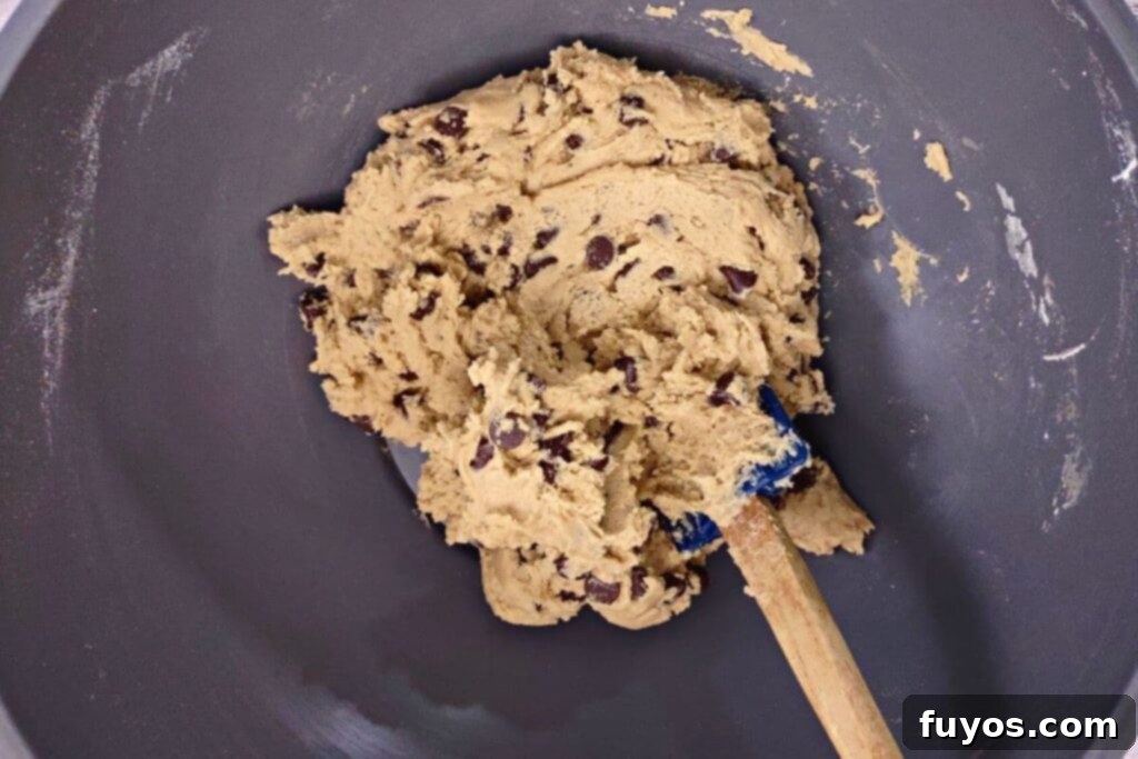 Chocolate chips being folded into the prepared cookie dough with a spatula