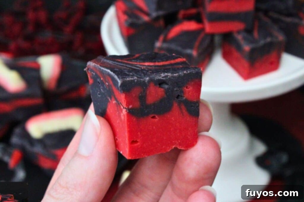 Vampire Fudge: A Sinfully Simple Halloween Indulgence 3 A hand holding a square of no-bake vampire fudge, highlighting the beautiful red and black swirls of the easy Halloween treat.