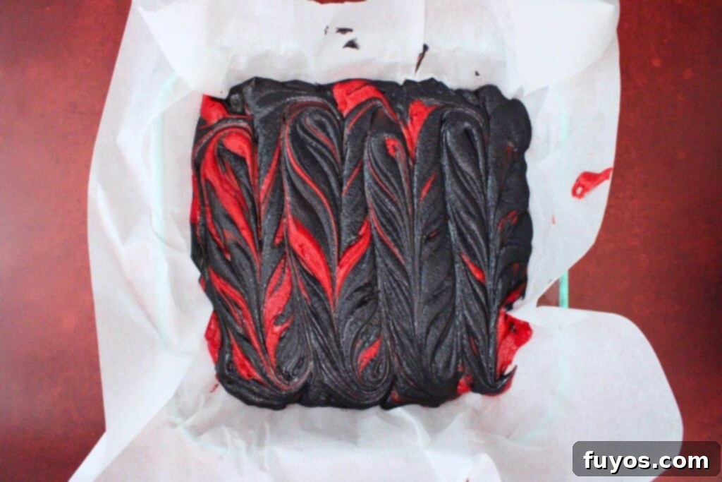 Vampire Fudge: A Sinfully Simple Halloween Indulgence 8 Red and black melted fudge mixtures poured into a parchment-lined pan, with a butter knife creating artistic swirls and marbling effects.