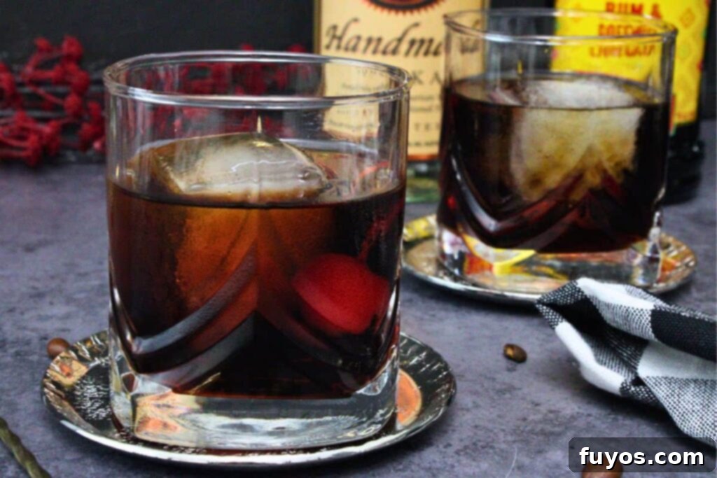 closeup view of two black russian cocktails with a cherry in lowball glasses on a dark counter