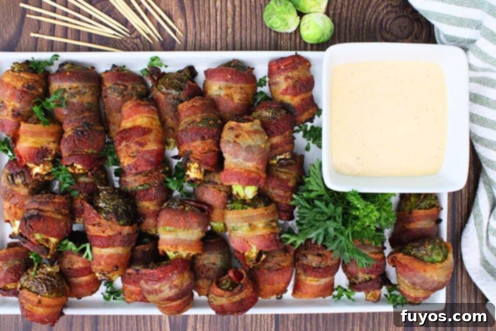 Overhead view of air fryer bacon wrapped brussel sprouts on a serving platter with a side of hot honey ranch dipping sauce