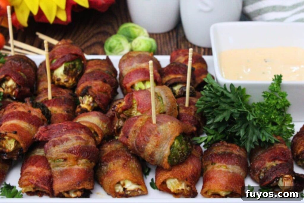 Air fryer bacon wrapped brussel sprouts spread across a serving platter with a side of hot honey ranch sauce