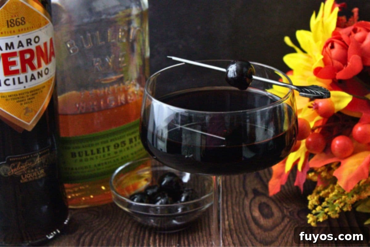 black manhattan cocktail up close with liquor bottles and flowers behind