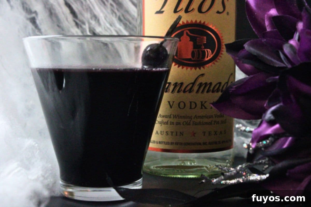 closeup side view of black martini drink in front of vodka bottle