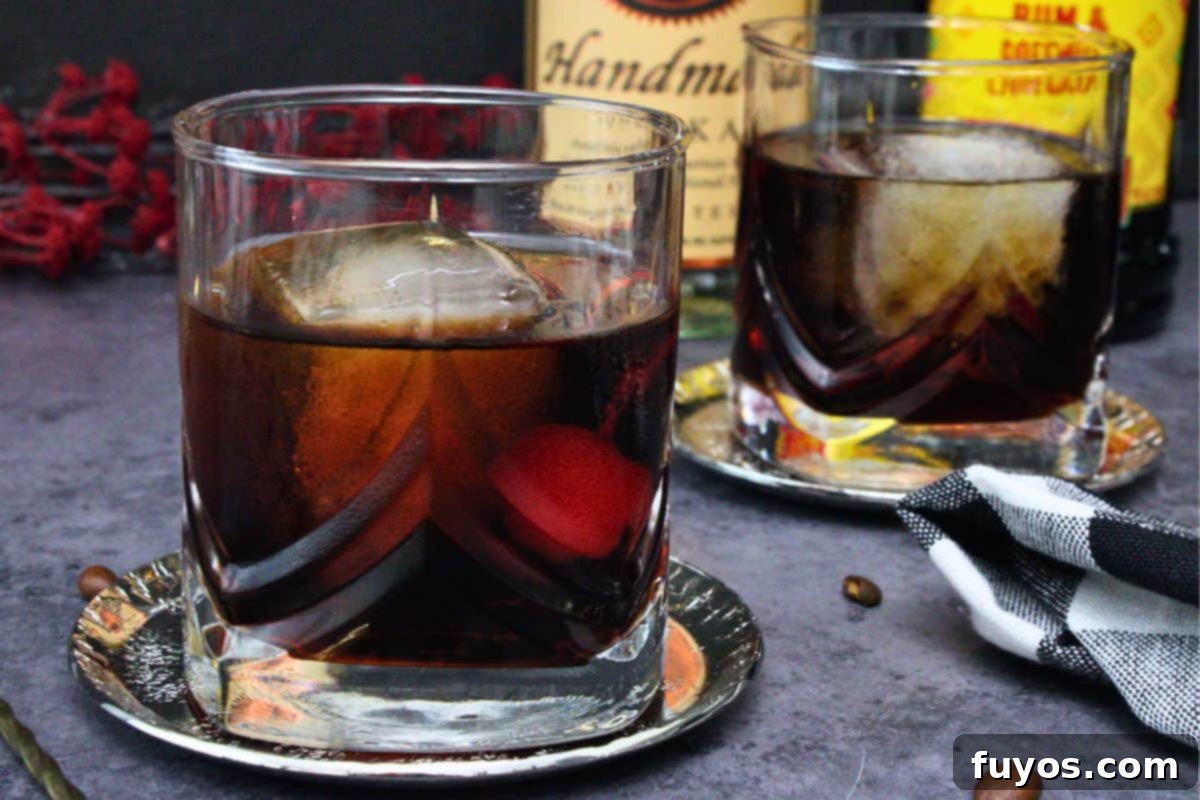 closeup view of two black russian cocktails with a cherry in lowball glasses on a dark counter