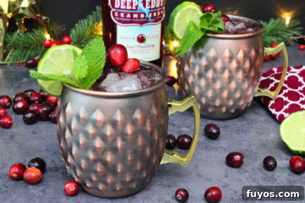 Cranberry Moscow Mule: Fall & Holiday's Signature Sip 9 two cranberry moscow mule drinks in copper mugs with lime and mint garnish and a vodka bottle in the background