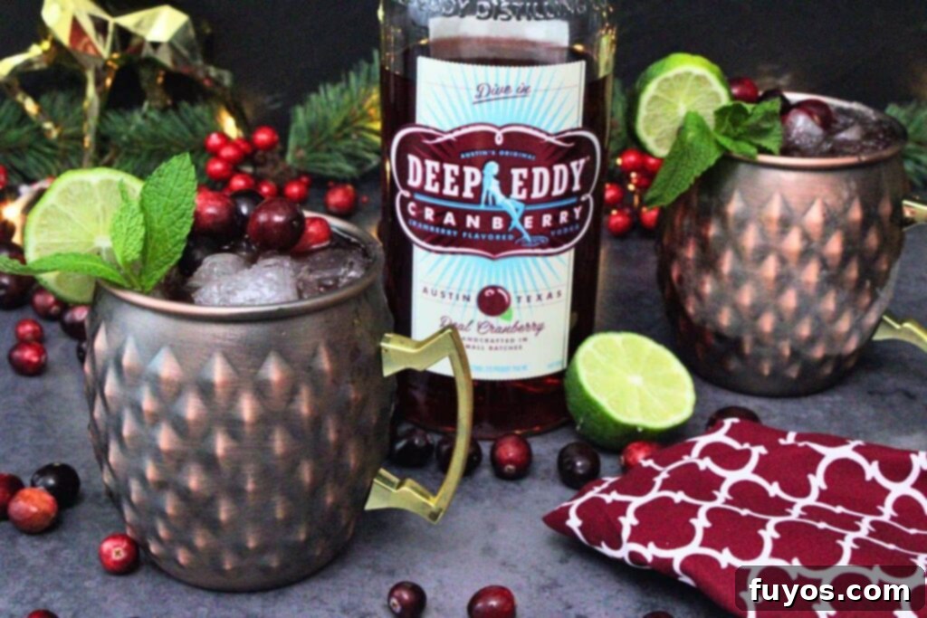 Cranberry Moscow Mule: Fall & Holiday's Signature Sip 3 cranberry moscow mule cocktail in a copper mug with mint and lime garnish next to vodka bottle surrounded by fresh cranberries
